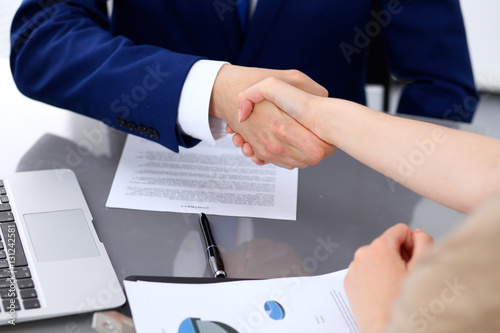 Businessman and business woman shaking hands to each other above signed contract