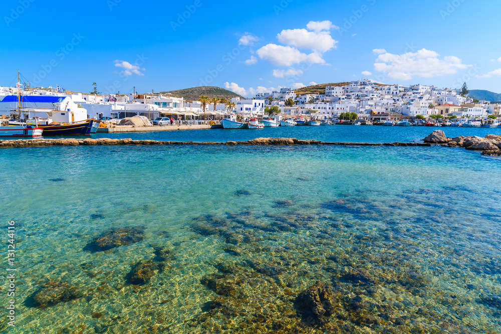 Crystal clear sea water in Naoussa bay with port in distance, Paros island, Greece
