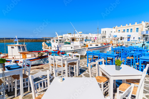 Restaurant tables and fishing boats anchoring in Naoussa port, Paros island, Greece