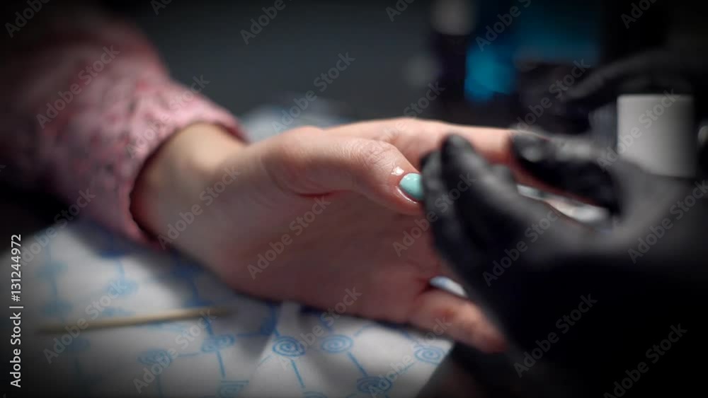 Manicurist in black gloves deals on fingers customer care cuticle oil close-up in bright light.