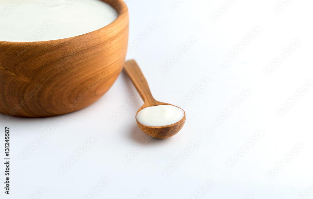 White yogurt in natural wooden bowl with wooden spoon on white background. White yogurt in natural wooden bowl with wooden spoon on white background.