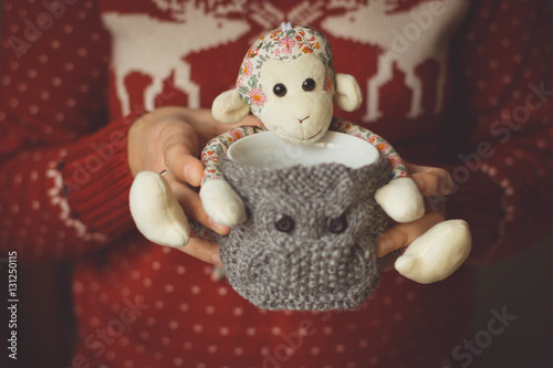 Knitted woolen cup with toy monkey in female hands