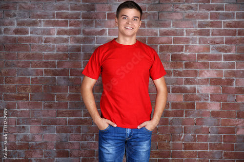 Handsome young man in blank red t-shirt standing against brick wall