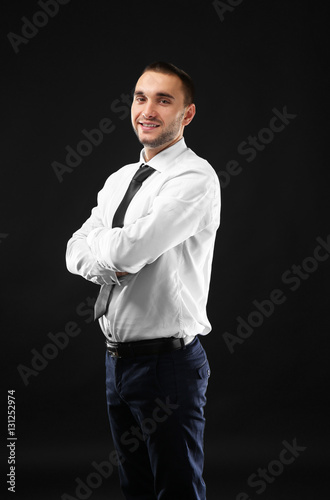 Young business coach with crossed hands standing on black background