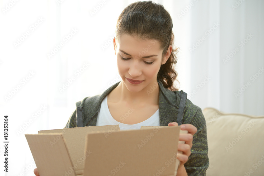Beautiful young woman opening box with parcel at home Beautiful young woman opening box with parcel at home