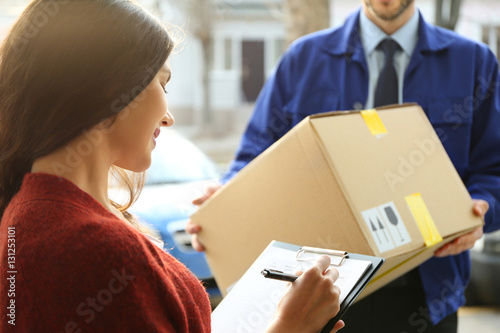 Young woman signing documents after receiving parcel from courier, closeup photo