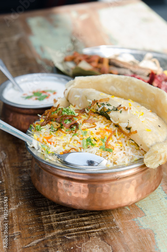 Authentic chicken biryani served with naan bread, fragrant pilau rice and yoghurt, in a metal pot... photo