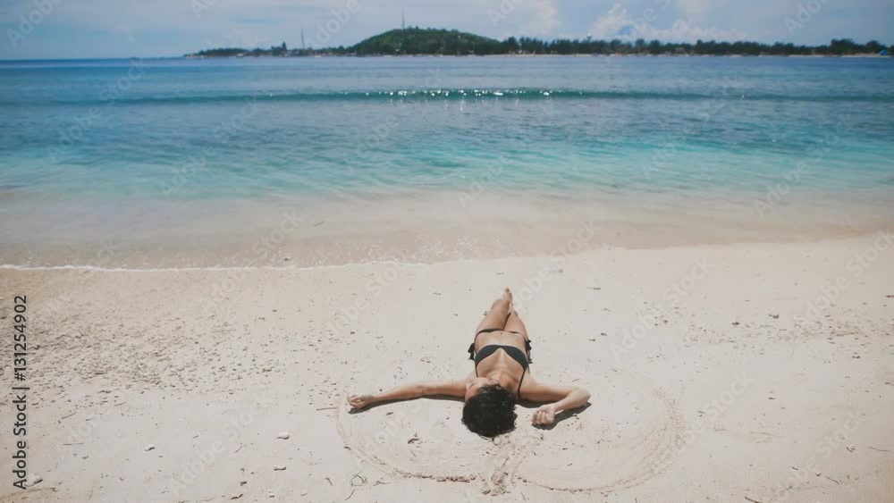 The beach on the island of Bali. Girl in a black bathing suit lying on a sandy beach and resting. Its soothing sand, sunny, clean and turquoise ocean island.