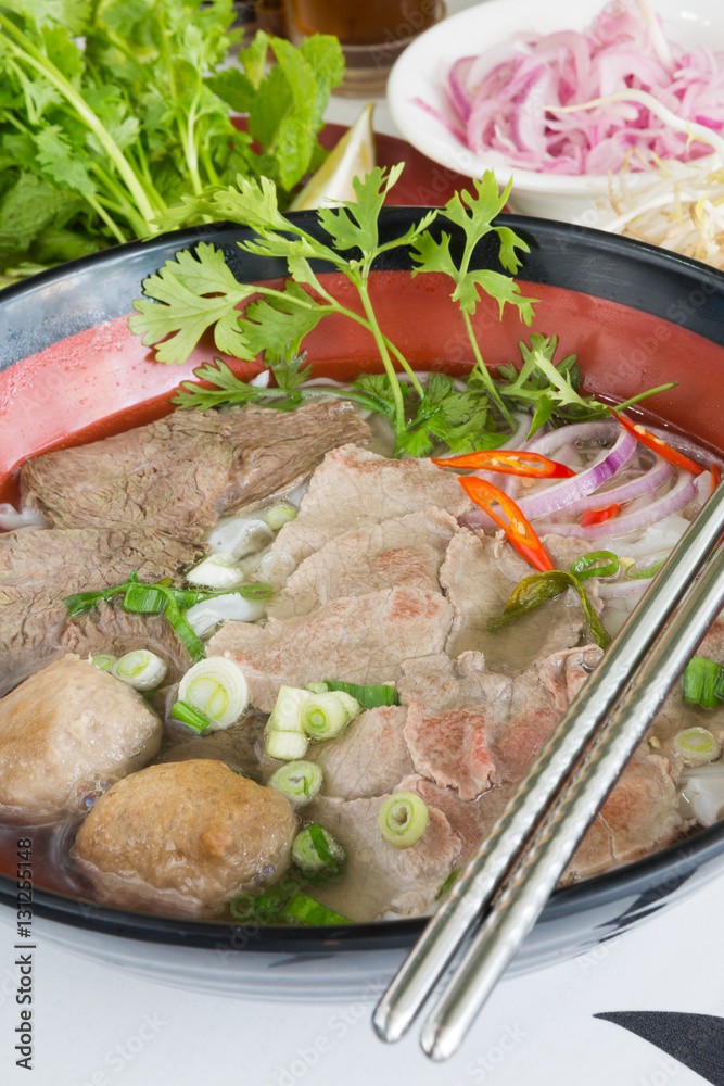 A bowl of traditional vietnamese beef and chicken pho street food, surrounded by fresh herbs. Pho is a vietnamese noodle soup consisting of meat, herbs, chilli, coriander and dumplings. A bowl of traditional vietnamese beef and chicken pho street food, surrounded by fresh herbs. Pho is a vietnamese noodle soup consisting of meat, herbs, chilli, coriander and dumplings.