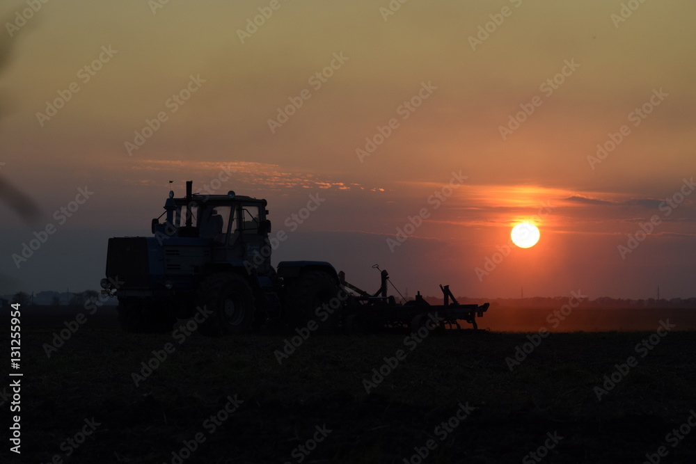 Tractor plowing plow the field on a background sunset. tractor silhouette on sunset background Tractor plowing plow the field on a background sunset. tractor silhouette on sunset background