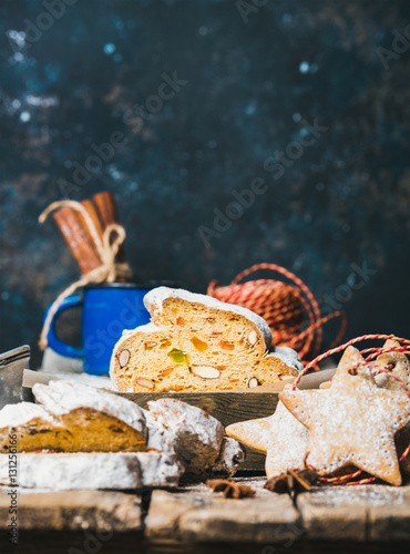 Piece of Traditional German Christmas cake Stollen with festive gingerbread star shaped cookies, selective focus, dark blue grunge background, copy space, vertical composition