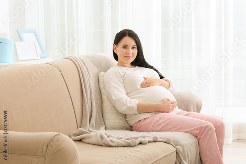 Beautiful young pregnant woman sitting on sofa at home