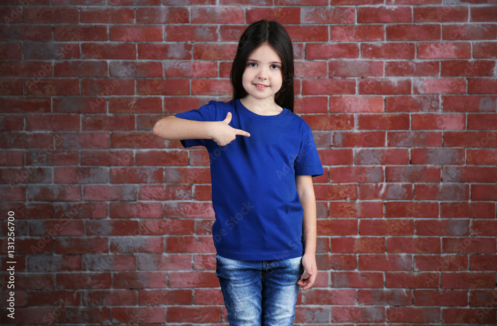 Little girl in blank blue t-shirt standing against brick wall Little girl in blank blue t-shirt standing against brick wall