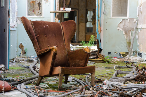 An old worn and damaged armchair, that has been left to rot in an abandoned building amongst concrete debris. photo