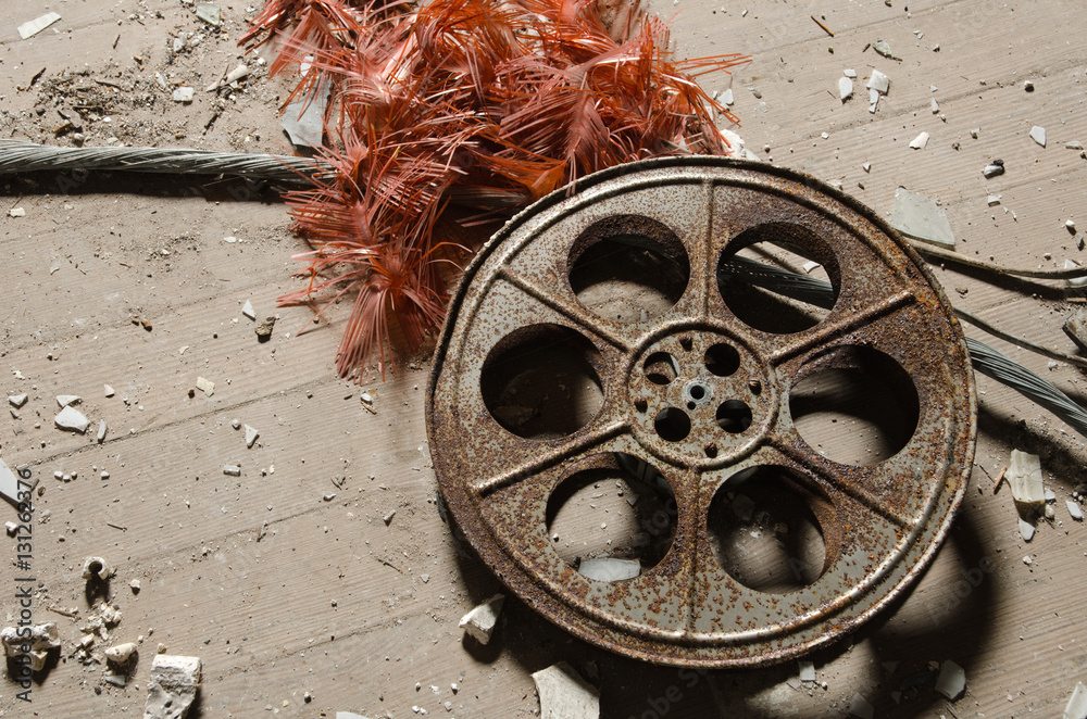 Fototapeta premium An old metal rusty cinematography cinema film reel, that has been left in an abandoned cinema amongst concrete debris.