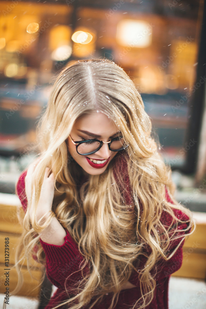 Blonde girl with glasses, smiling in a burgundy sweater, snow, winter