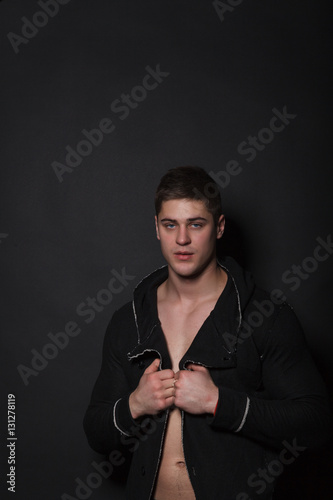 Fashionable man standing on a black background. Muscular man in black sweater