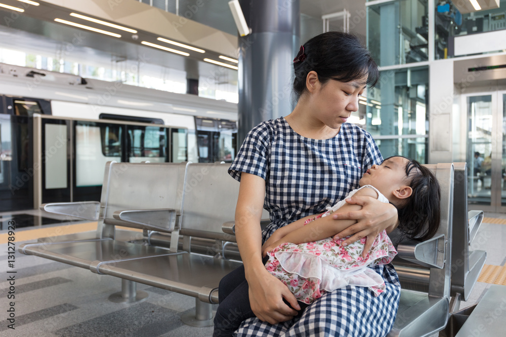 Asian Chinese mother carrying sleeping daughter inside a MRT sta Asian Chinese mother carrying sleeping daughter inside a MRT sta