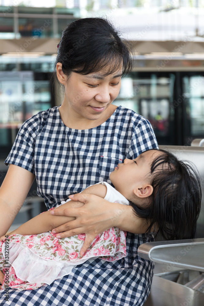 Asian Chinese mother carrying sleeping daughter inside a MRT sta Asian Chinese mother carrying sleeping daughter inside a MRT sta