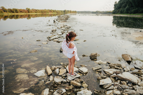 a little girl standing on stones by the river