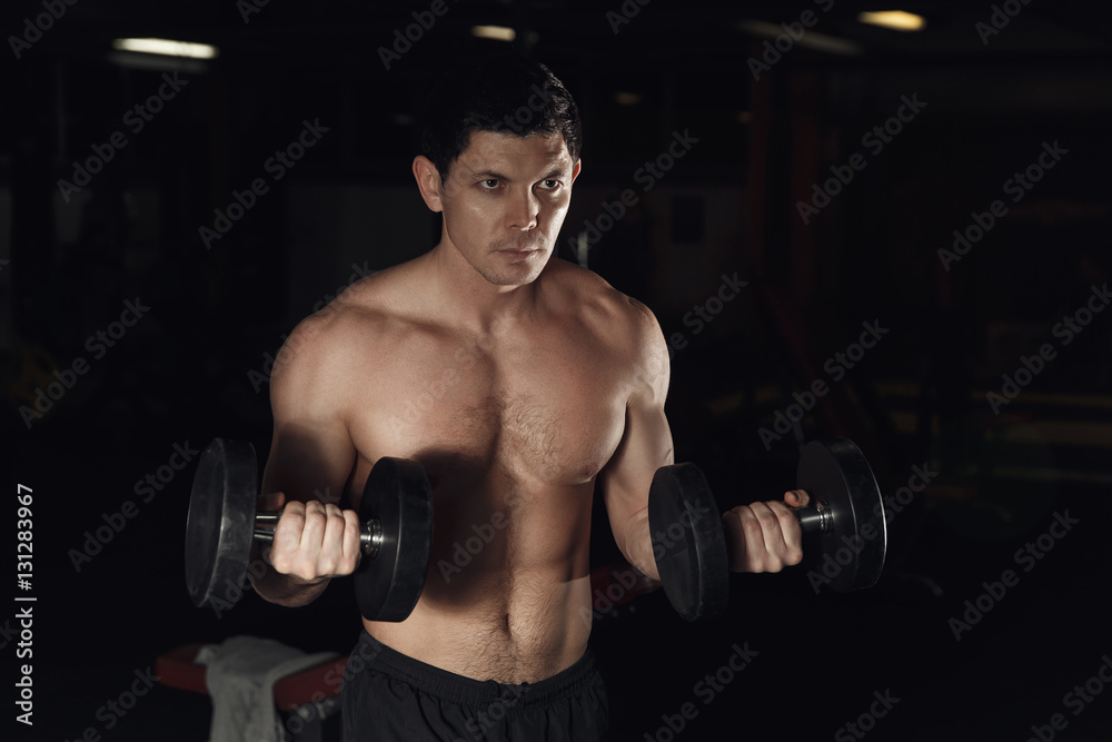 very power athletic guy bodybuilder, execute exercise with dumbbells, in dark gym.