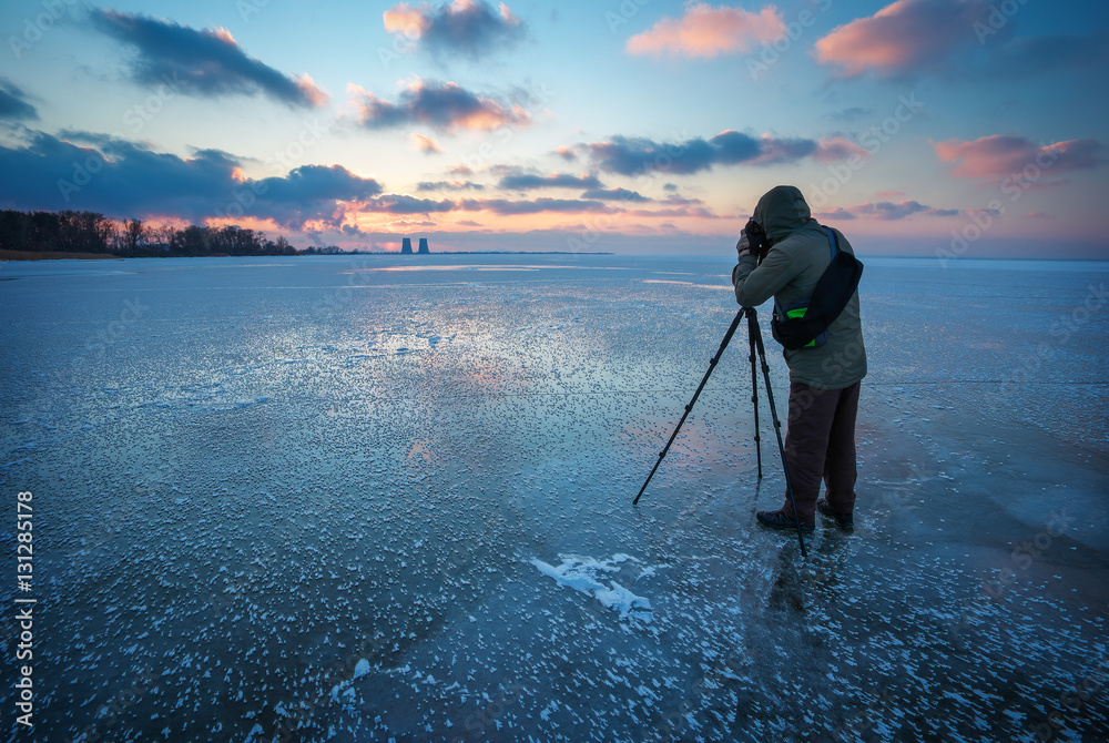 Photographer takes a picture of sunset on a frozen river in winter