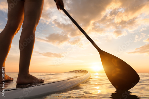 Stand up paddle boarding on quiet sea, legs close-up, sunset photo