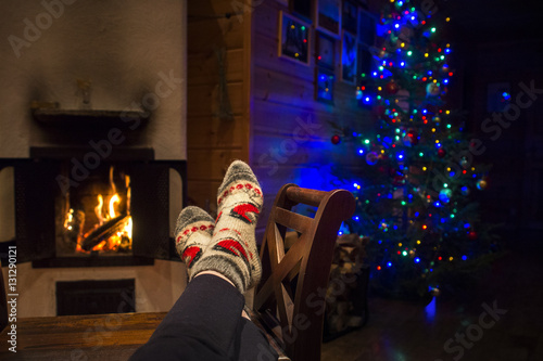 woman is warming her legs near the fireplace in wooden country house during christmas holidays