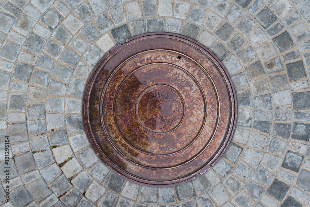 Closeup photo of Old Sewer rust manhole cover on the urban asphalt road. Rain scene.