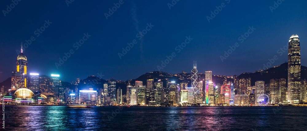Fototapeta premium ​Hong Kong, China skyline panorama from across Victoria Harbor. Hong Kong city skyline view from harbor with skyscrapers buildings reflect in water at sunset