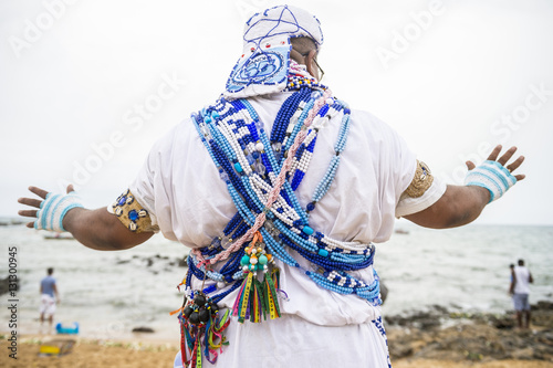 A Brazilian candomble priest performs a blessing at the Festival of Yemanja in traditional blue and white robes with colorful beads on the beach at Rio Vermelho in Salvador, Bahia, Brazil