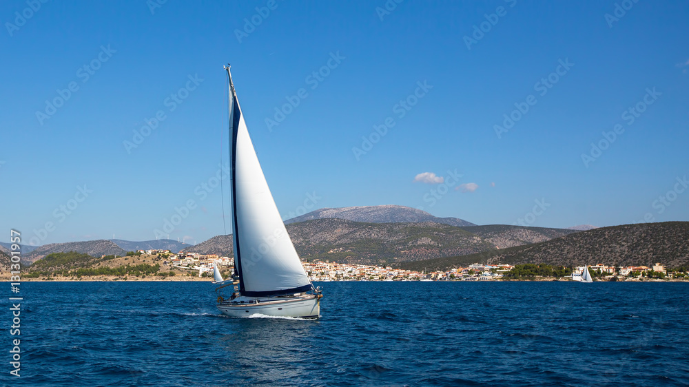 Fototapeta premium Sailboat with white sails in the Aegean sea near Greece coasts. Sailing, luxury yachts.