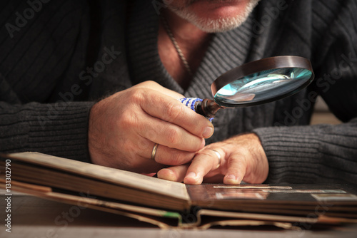 Man considers album of stamps trough the magnifying glass horizontal