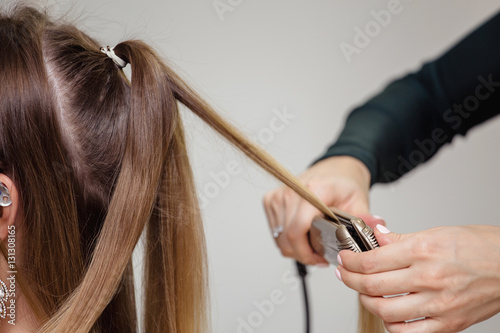 Hairdresser working with beautiful woman brown hair in hairdressing salon. Close up view of hand, ripple curling iron