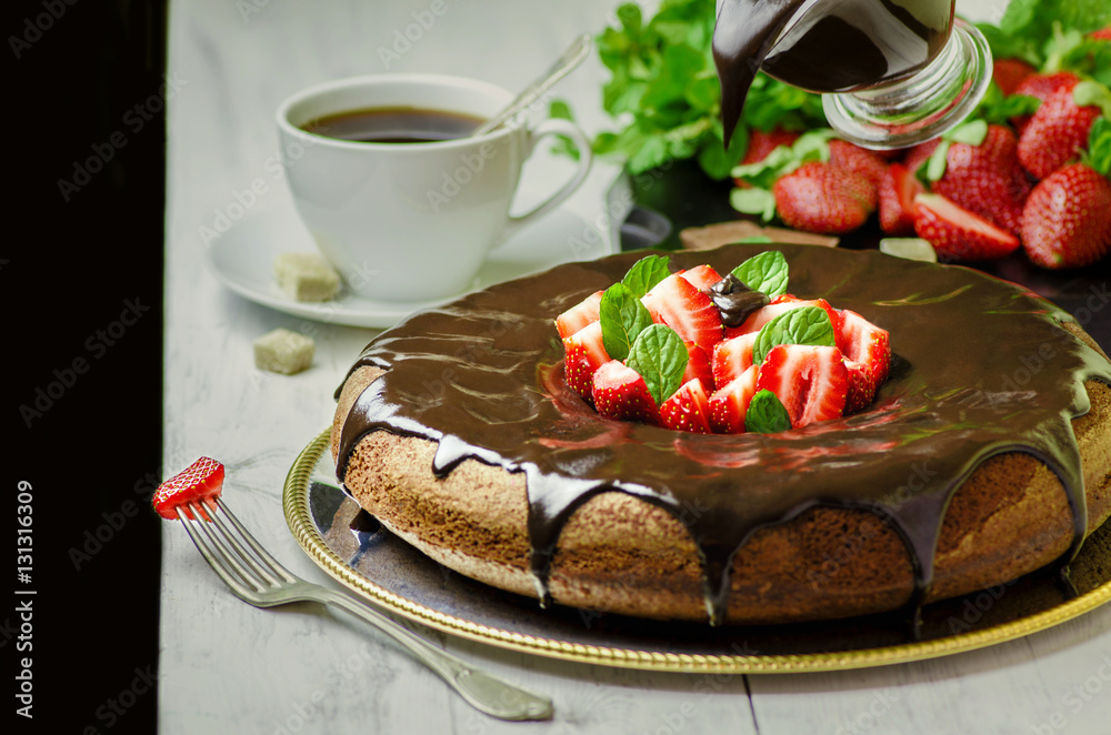 Φωτογραφία Pouring chocolate sauce on delicious chocolate cake with fresh strawberries,cup of tea and mint on white wooden background
