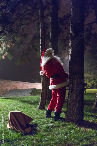 Rude and drunk Santa Claus pee in the park. photo