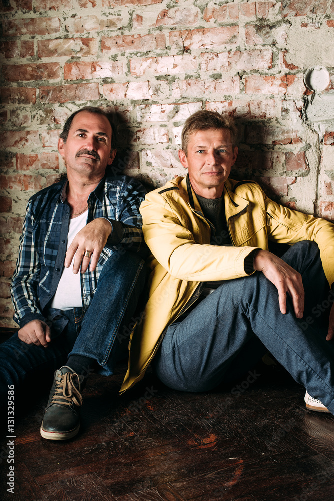 Two handsome middle aged men, dressed in casual clothing , old friends. Red brick wall background.