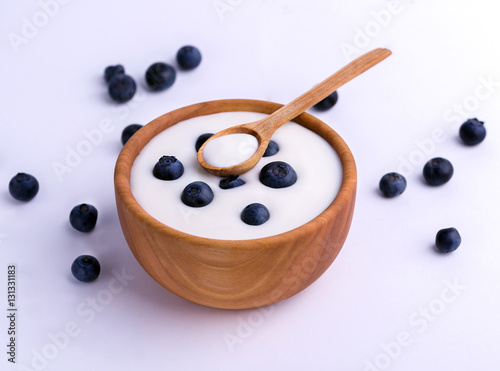 White yogurt in natural wooden bowl with blueberries on isolated white background.