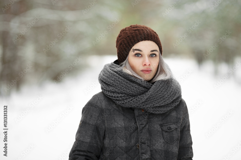 Young adorable frown blonde hipster woman with pierced eyebrow wearing grey plaid coat having fun in snowy winter forest outdoors. Nature cold season freshness concept. Young adorable frown blonde hipster woman with pierced eyebrow wearing grey plaid coat having fun in snowy winter forest outdoors. Nature cold season freshness concept.