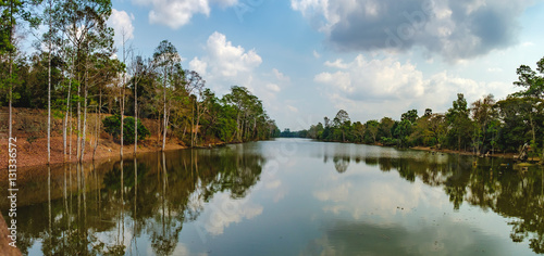 Beautiful lake nestled among rainforest in Cambodia under blue sky with white clouds. It surrounding mysterious ruins of Angkor Thom in Siem Reap, Cambodia.