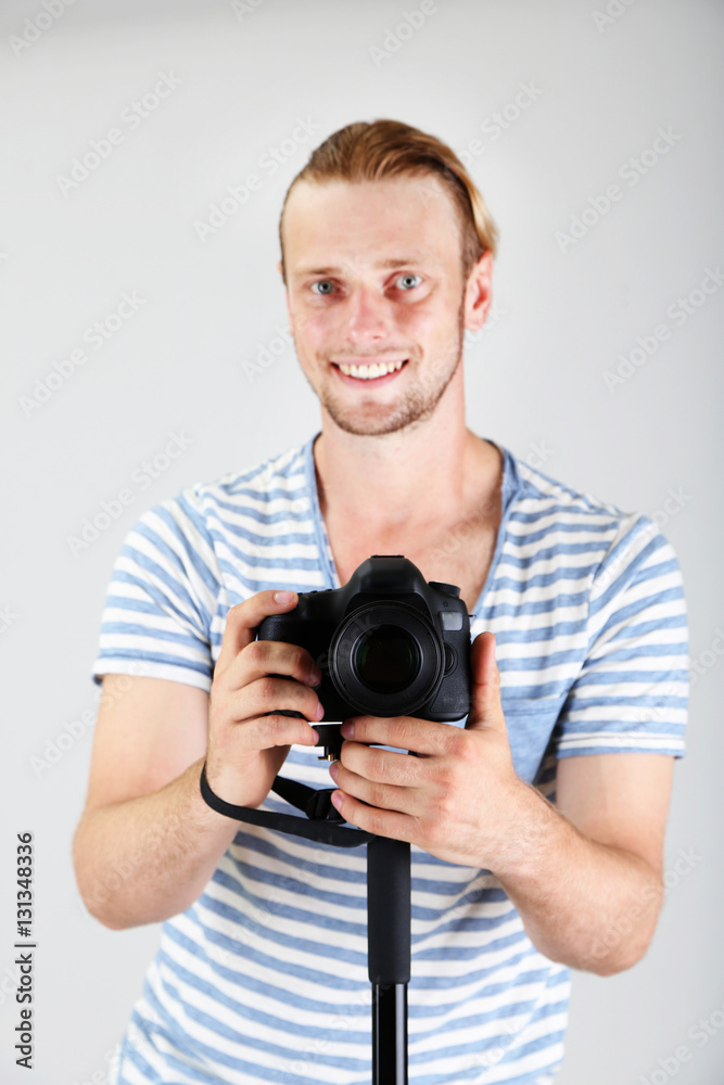 Handsome photographer with camera on monopod, on gray background