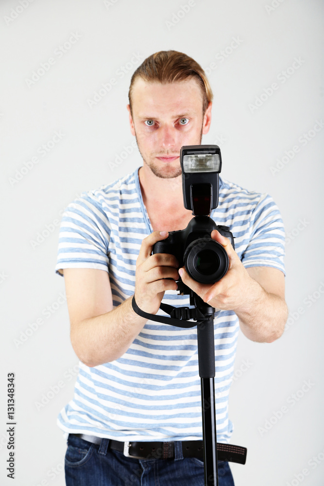 Obraz premium Handsome photographer with camera on monopod, on gray background