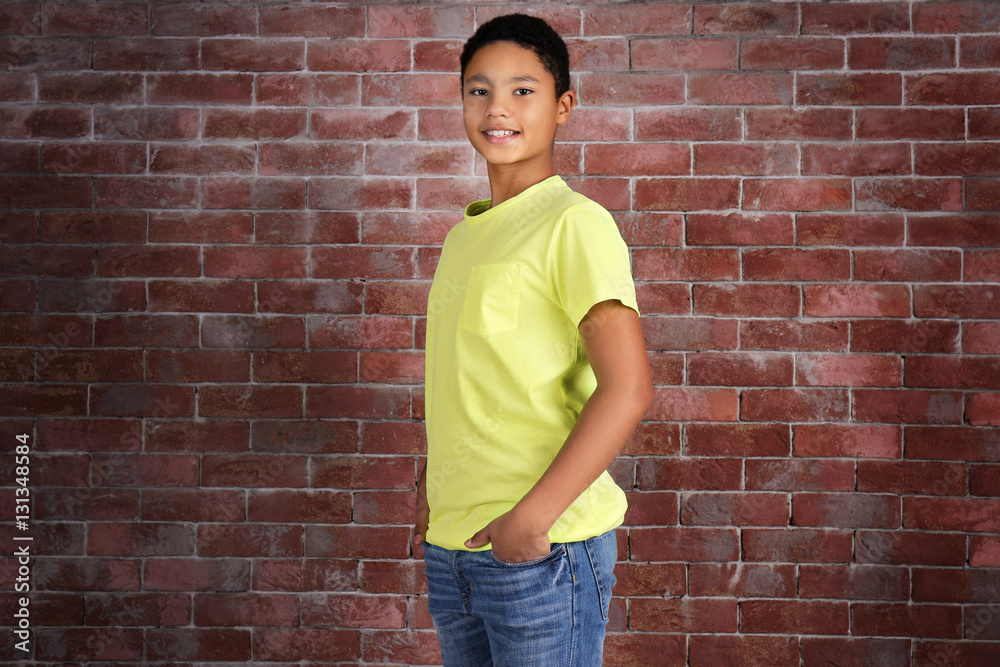Young African American boy in blank yellow t-shirt standing against brick wall