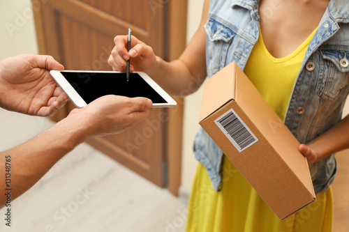 Young woman appending signature after receiving parcel from courier at home, closeup