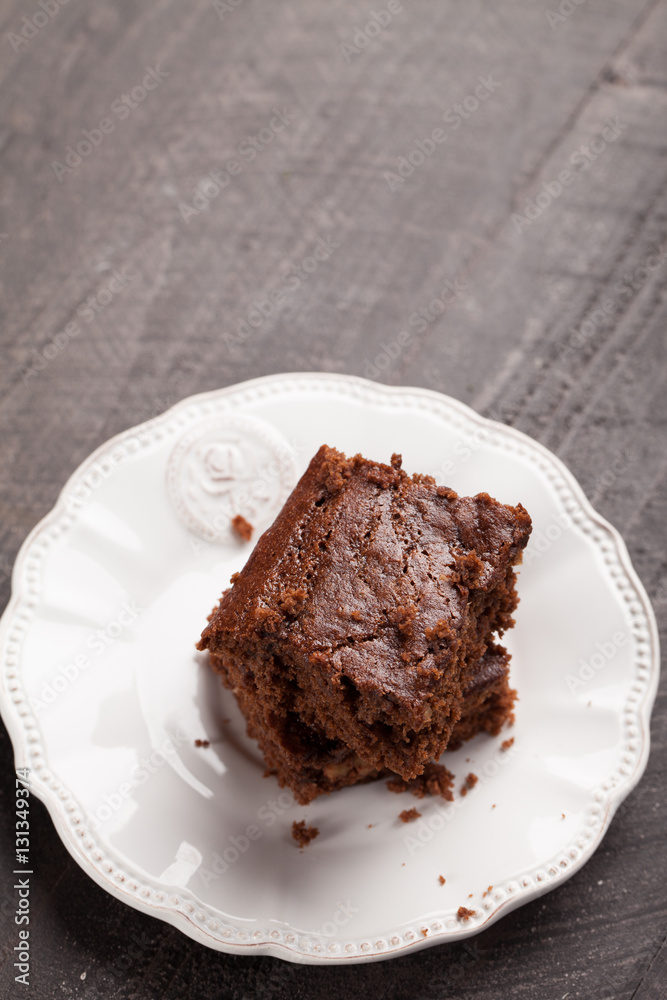 Walnut brownie cake stacked on white plate on dark wooden background angled shot