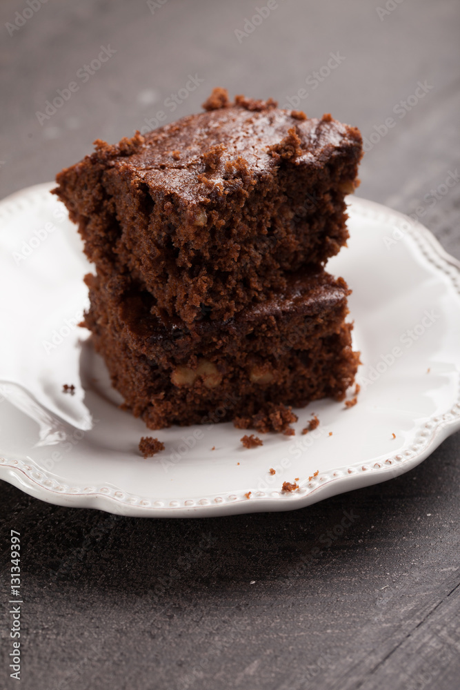 Walnut brownie cake stacked on white plate on dark wooden background slightly above shot