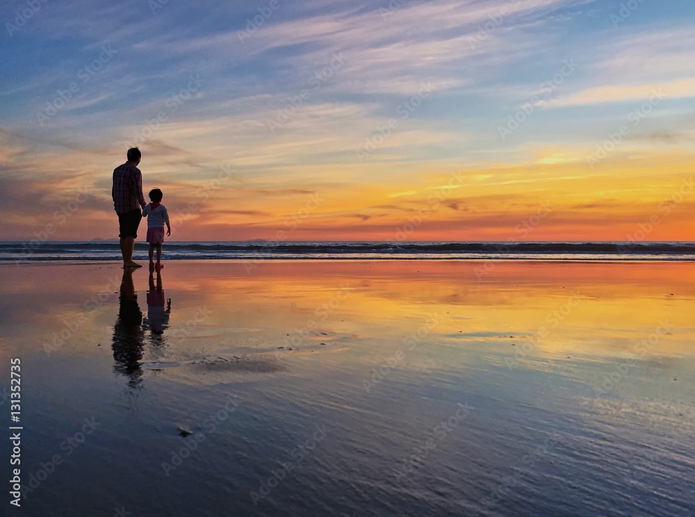 Silhouette of father and child at beach shoreline during sunset
