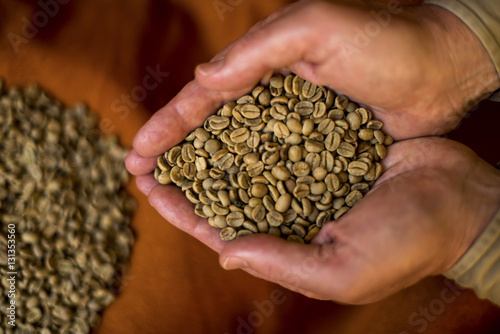 Handful raw coffee beans tipped top more table.