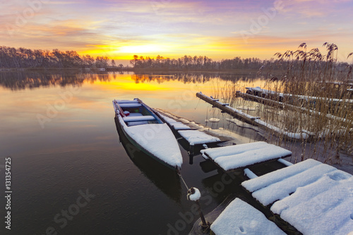 boat moored to the snow-covered bridge over the lake in winter m