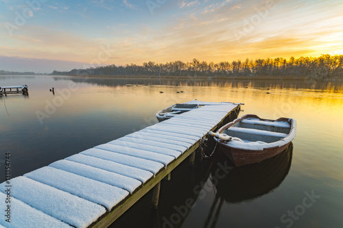 Fototapeta Naklejka Na Ścianę i Meble -  boat moored to the snow-covered bridge over the lake in winter m
